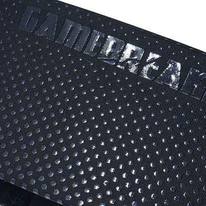Close-up of a black textured fabric strap with a repeating circular dot pattern and a debossed metallic logo reading 'GAMEBREAKER' across the top edge.