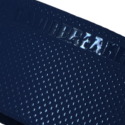 Close-up of a dark navy blue athletic mesh fabric with a repeating perforated pattern and a reflective metallic logo reading 'GAMEBREAKER' across the waistband.